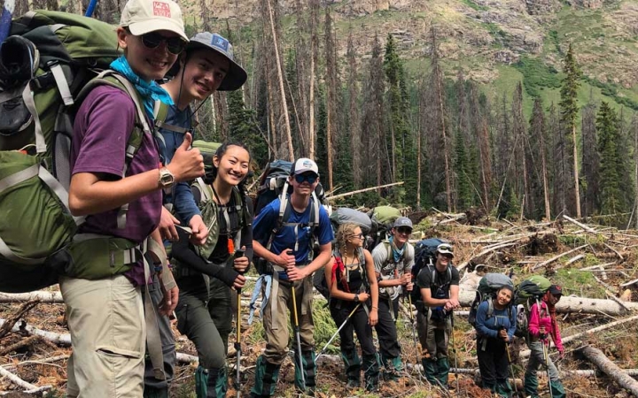 a group of backpacking students smile at the camera amongst felled trees
